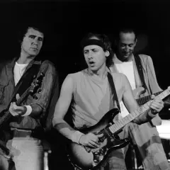 Trzech członków Dire Straits gra na gitarach podczas koncertu.