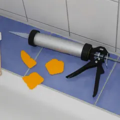 Pistolet do silikonu, szpachelki i drewniana łopatka gotowe do wymiany silikonu w kabinie prysznicowej.