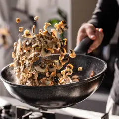 Man salteando champiñones en una sartén, mostrando cómo cocinar las setas para un plato delicioso.
