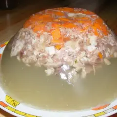 Tradycyjna galareta wieprzowa z kawałkami mięsa i marchewki, w galaretce, na talerzu.