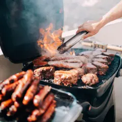 Leckeres Grillen auf dem Balkon: Würstchen und Steaks brutzeln auf dem Rost, Flammen lodern.
