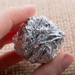 Dłoń trzyma kulkę z pogniecionej folii aluminiowej, która może być szkodliwa.