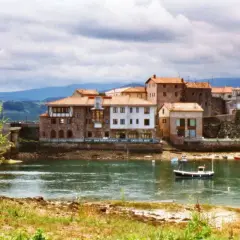 Pueblos de Cantabria con playa, casas de piedra y tejados rojos junto a un río tranquilo con barcas.