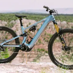 A light blue specialized levo 4 electric mountain bike is parked on a rocky trail with a scenic canyon in the background.