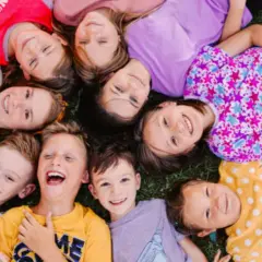 Niños sonriendo y jugando juntos en la hierba, una escena alegre de escuela de verano para niños de 2 años.