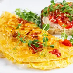 Złocisty omlet z pomidorami, posypany sezamem, podany z tostami i kiełkami. Pyszne śniadanie.