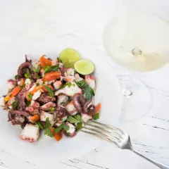 Frischer oktopus salat mit Tomaten, Petersilie und Limette, daneben ein Glas Weißwein.