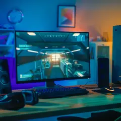 Bureau de jeu avec PC puissant, écran affichant un jeu vidéo, clavier, souris et casque. Ambiance lumineuse, parfait pour config windows 11.