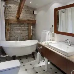 Łazienka z wanną wolnostojącą i kamienną ścianą. Duże lustro łazienkowe retro nad umywalką dodaje uroku.