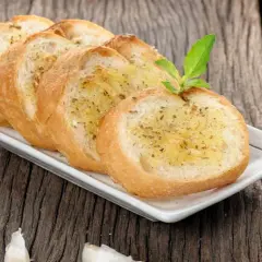 Tranches de pain grillé à l'ail, garnies d'herbes, rappelant la préfou recette traditionnelle. Une tête d'ail repose à côté.