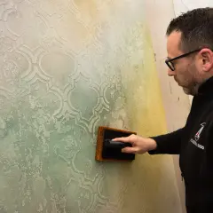 Un artigiano applica pittura per marmo su una parete con un motivo a rombi, creando un effetto materico e anticato.