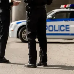 Policjanci w pełnym umundurowaniu stoją obok radiowozu. Ich wyposażenie jest gotowe do akcji.