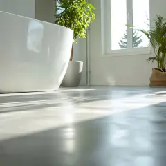Solen lyser upp ett modernt badrum med fristående badkar och växter. Golvet är av microcement på våtrumsmatta, vilket ger en stilren och hållbar yta.
