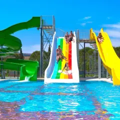 Wesoła zabawa na zjeżdżalniach wodnych w Venosa Beach Resort & Spa. Dzieci i dorośli ścigają się po tęczowej i żółtej zjeżdżalni, wpadając do basenu.
