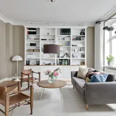 Stilvolle wandgestaltung wohnzimmer mit einem weißen Bücherregal, Ledersesseln und einem grauen Sofa.
