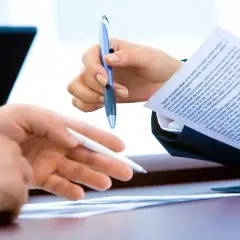 Dwie osoby omawiają dokumenty, być może umowa kompleksowa Tauron. Jedna trzyma niebieski długopis, druga biały.