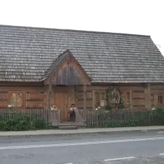 Drewniany budynek muzeum powstania chochołowskiego z gontowym dachem. Dzieci siedzą na progu.