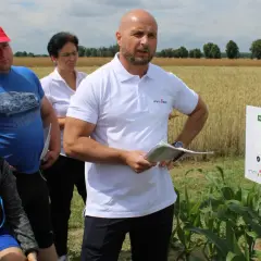 Grupa ludzi na polu kukurydzy, gdzie prezentowane są środki ochrony roślin, w tym metkonazol.