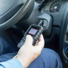 Ręka trzymająca skaner diagnostyczny OBD w samochodzie.