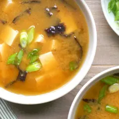 Two bowls of steaming nori soup, filled with tofu cubes and green onions, are ready to be enjoyed.