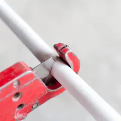 A red pipe cutter is shown in action, demonstrating how to cut PVC pipe cleanly and efficiently.