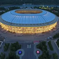 Oświetlony moskiewski stadion w nocy, z widokiem na rzekę i otaczający go las.