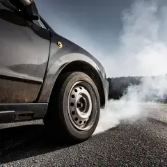 Une voiture freine brusquement, dégageant une épaisse fumée blanche. L'odeur de brûlé de plaquette de frein neuve emplit l'air.