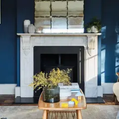 Ein gemütliches Wohnzimmer mit tiefblauen Wänden. Gelbe Akzente auf dem Tisch und Kissen zeigen, welche Farbe passt zu Blau und bringt Wärme.