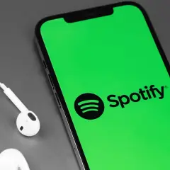 Telefon z zielonym ekranem i logo Spotify, obok białe słuchawki. Słuchaj muzyki za darmo dzięki Spotify free.