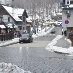 Zimowy deptak w Szklarskiej Porębie, z samochodami na ulicy i sklepikami po bokach.