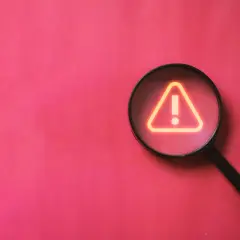 Lupa powiększa znak ostrzeżenia, symbolizując analizę różnych rodzajów funkcji i potencjalnych problemów.