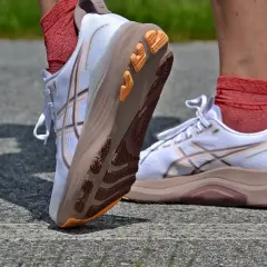 Białe buty do biegania Asics z pomarańczowymi akcentami na podeszwie. Firma Asics słynie z innowacyjnych rozwiązań.