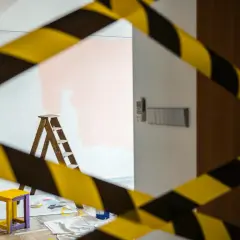 Cinta de precaución amarilla y negra rodea una habitación con una escalera, un taburete y pintura rosa en la pared, ilustrando la diferencia entre obras de mejora y obras de conservación.