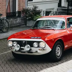 Czerwone auto sportowe Alfa Romeo z lat 70. na brukowanej ulicy, obok rower.