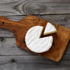 Un morceau de **brie** crémeux, avec une part coupée, sur une planche en bois rustique.
