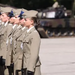 Żołnierz zawodowy w mundurze stoi w szeregu. W tle widać czołg.