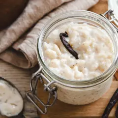 Un pot en verre rempli de riz au lait au four, garni d'une gousse de vanille. Une cuillère à côté en témoigne.