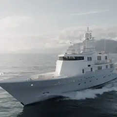 L'alessandro del bono yacht solca le onde con eleganza, un gioiello bianco su un mare calmo, con montagne sullo sfondo.
