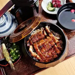 Pyszny unagi na ryżu, podany z dodatkami: chrzanem, szczypiorkiem, marynowanymi warzywami i zupą.
