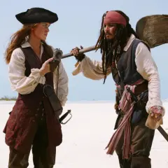 Elizabeth Swann i Kapitan Jack Sparrow, bohaterowie filmów "Piraci z Karaibów", stoją na plaży, rozmawiając.