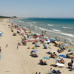 Gente disfrutando de un día soleado en las playas de la marina, con sombrillas de colores y el mar azul de fondo.