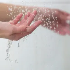Manos bajo un chorro de agua fría, sintiendo el frescor al ducharse con agua fría.