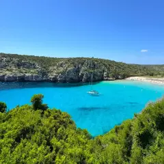 Rajskie minorka plaże z turkusową wodą, łodzią żaglową i skalistymi klifami.