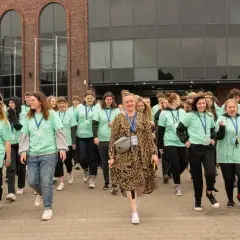 Grupa młodych ludzi w zielonych koszulkach idzie przed budynkiem z cegły.
