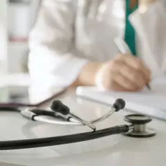 Lekarz rodzinny wypisuje receptę L4 na depresję. Na biurku leży stetoskop.