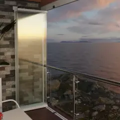 Balcone con vepa edilizia libera, vista mare al tramonto. Pianta in vaso e arredi moderni.