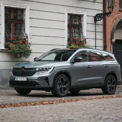 Nowy Renault Espace 2024 w szarym kolorze na brukowanej uliczce, z kwiatami w oknach.