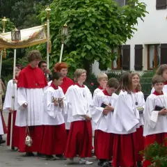 Prozession am Corpus Christi Feiertag mit Ministranten in weißen und roten Gewändern, die eine Monstranz tragen.