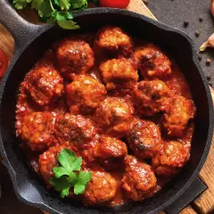 Pyszne pulpety z indyka w sosie pomidorowym, podane w żeliwnej patelni, z dodatkiem czosnku, pomidorów i natki pietruszki.