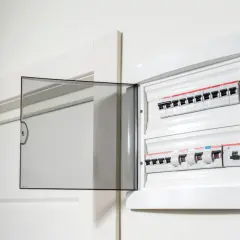 Otwarta biała skrzynka z bezpiecznikami elektrycznymi na ścianie.